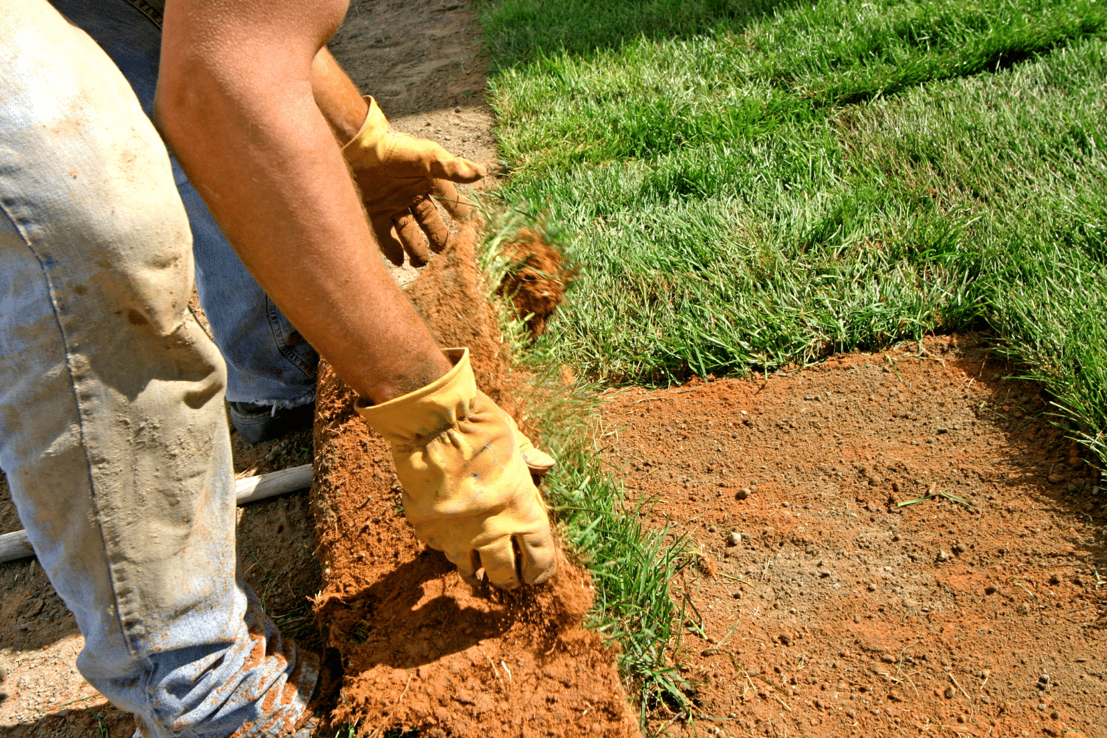 Person installing artifical grass in a yard, smoothing out the surface for a neat and even finish.